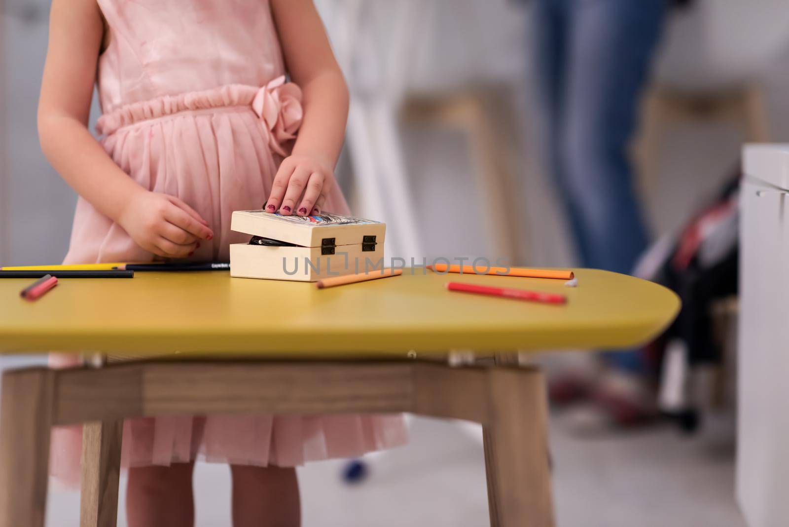 happy family spending time together at home  cute little daughter in a pink dress playing and painting the jewelry box while young redhead mother ironing clothes behind her