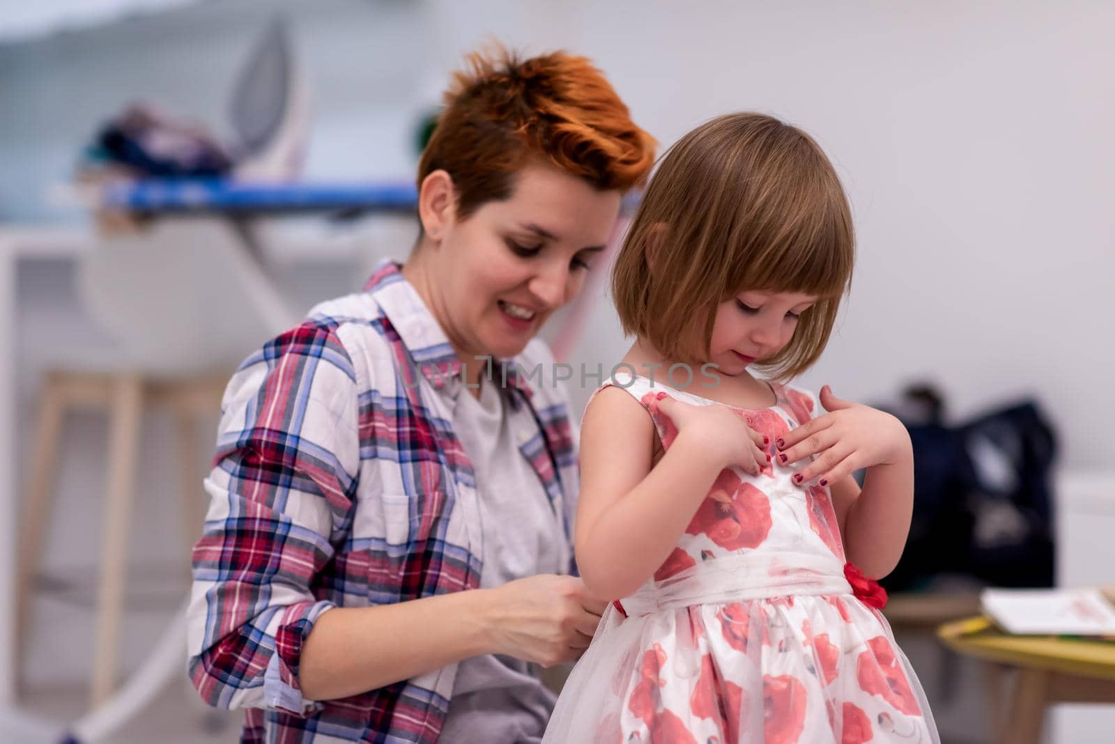 mother helping daughter while putting on a dress by dotshock