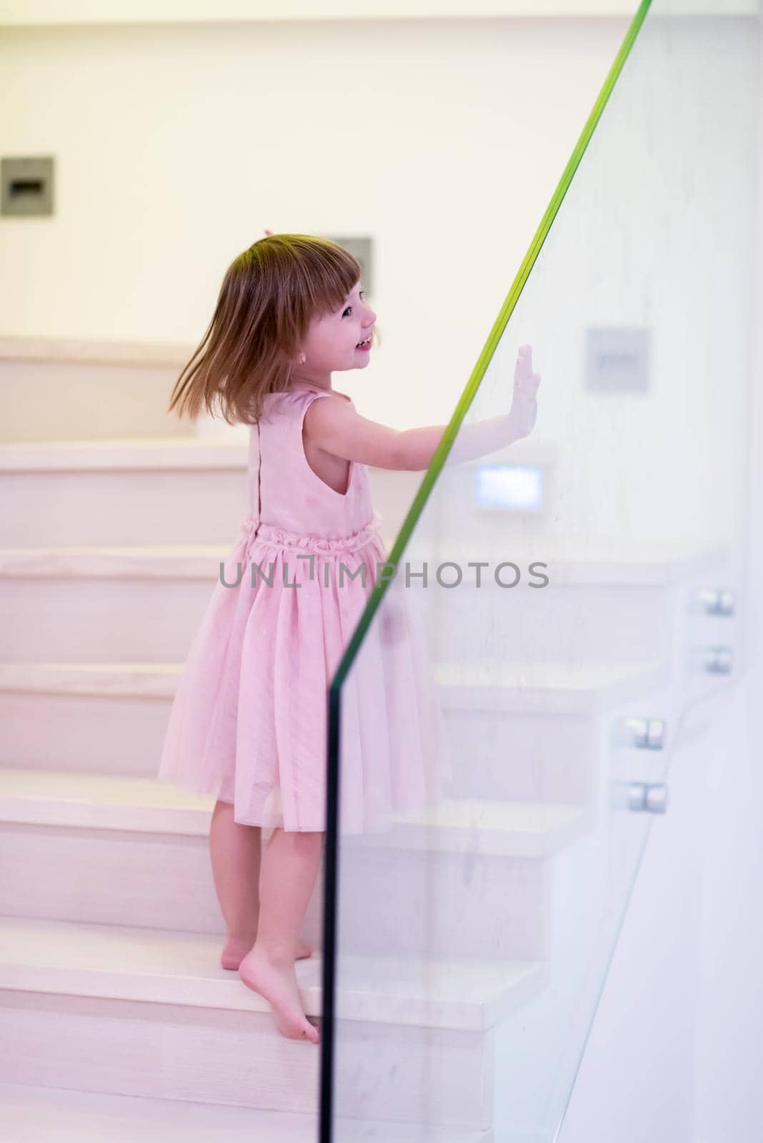happy cute little girl in pink dress enjoying while playing on wooden stairs at stylish two level apartment