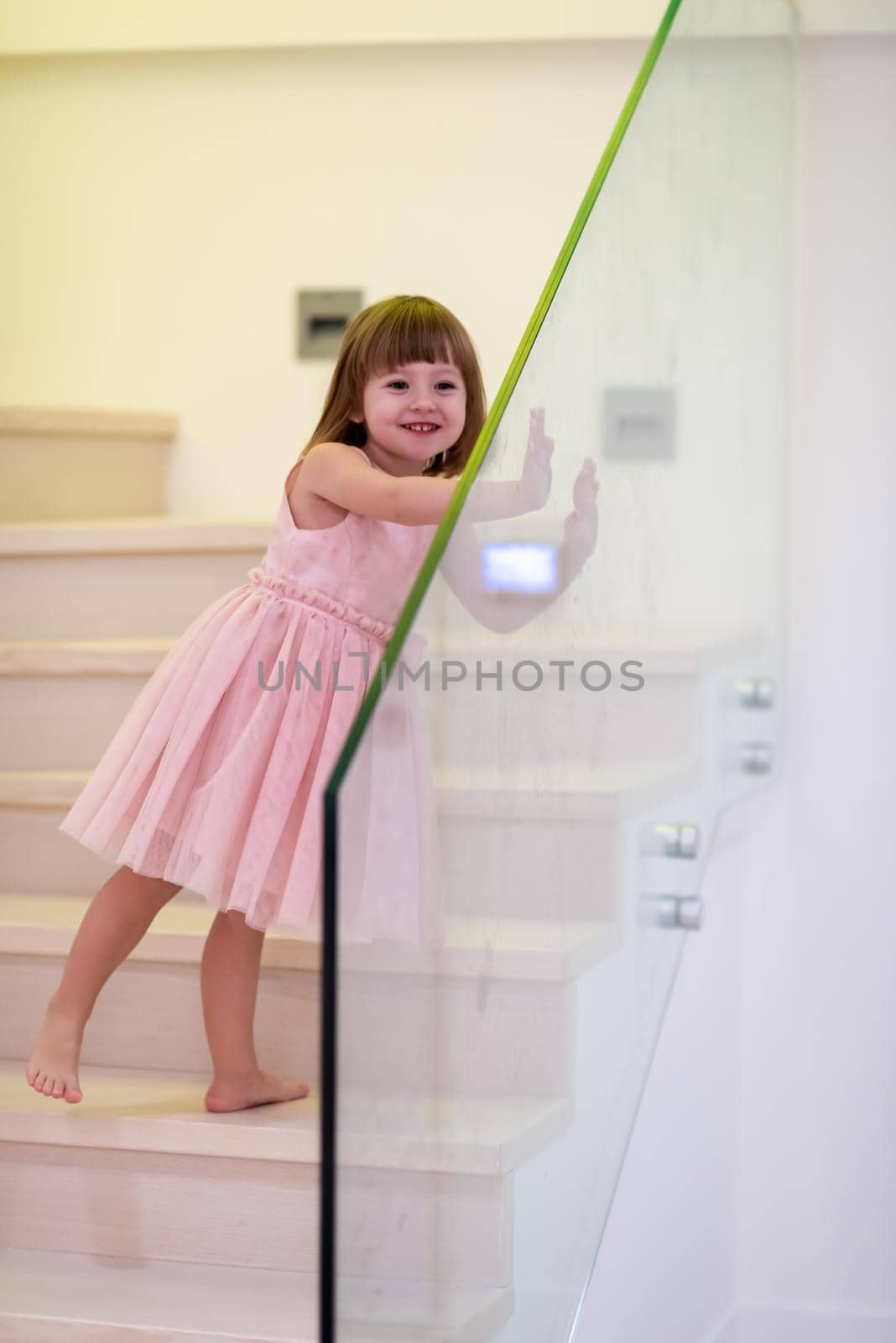 happy cute little girl in pink dress enjoying while playing on wooden stairs at stylish two level apartment