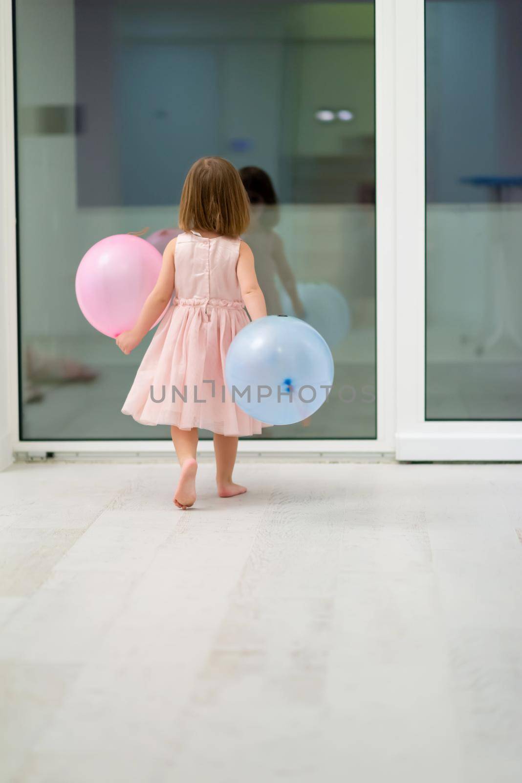 happy cute little girl in a pink dress enjoying while playing with balloons on beautiful evening near the window at home