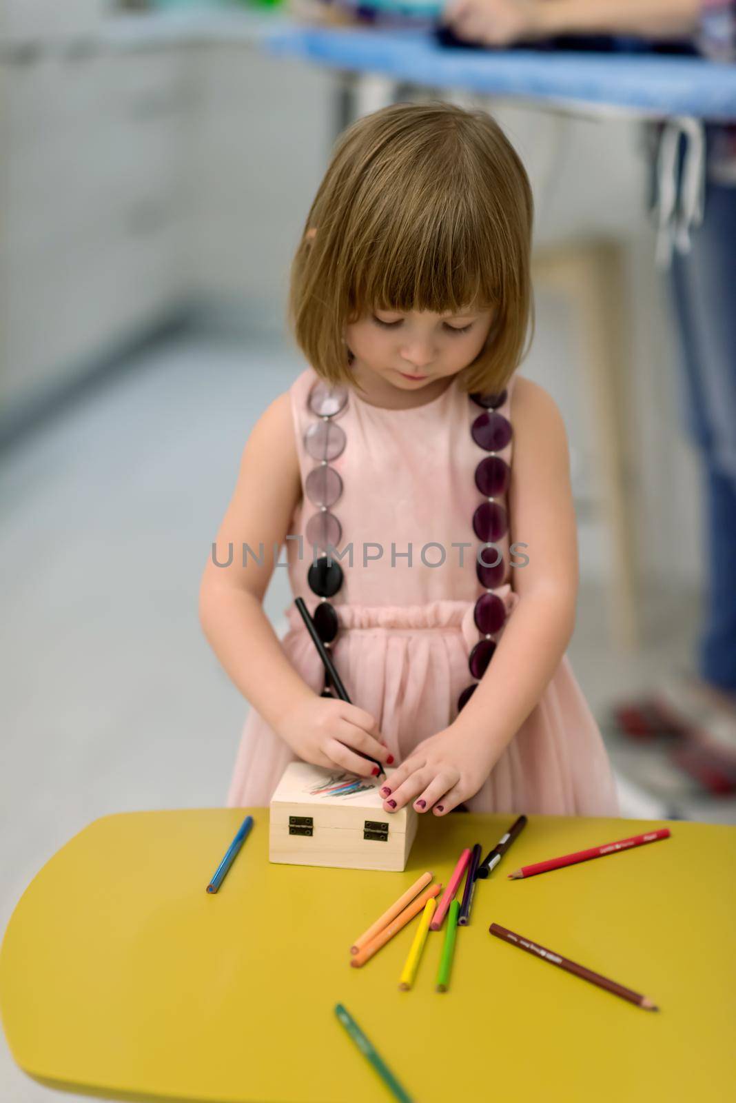 happy family spending time together at home  cute little daughter in a pink dress playing and painting the jewelry box while young redhead mother ironing clothes behind her