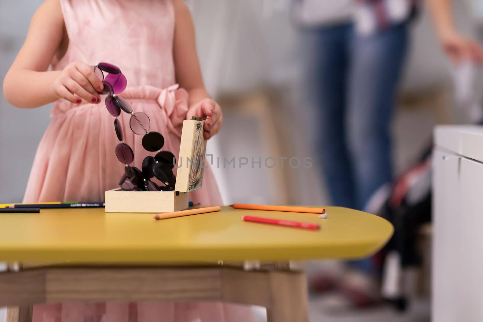 happy family spending time together at home  cute little daughter in a pink dress playing and painting the jewelry box while young redhead mother ironing clothes behind her