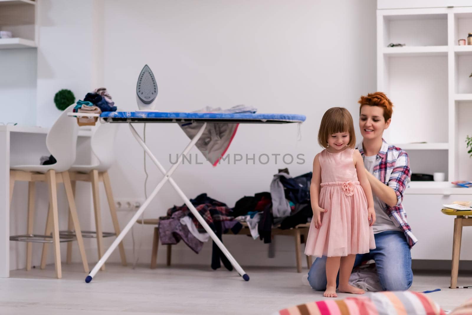 mother helping daughter while putting on a dress by dotshock