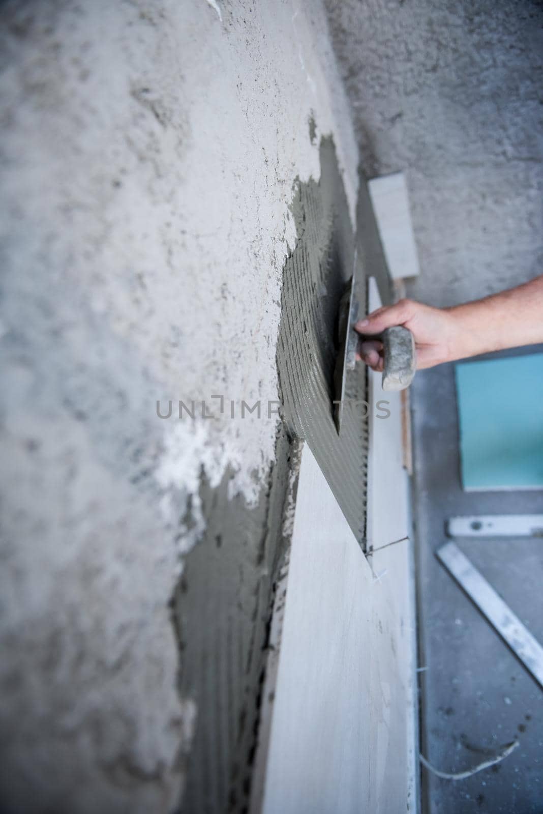 experienced senior construction worker installing big ceramic tiles on interior concrete walls