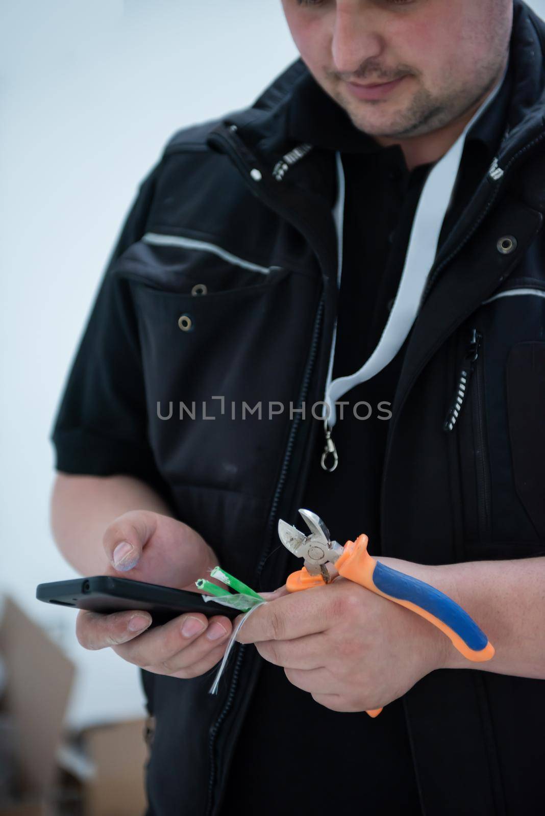 electrical engineer with wire and pliers in his hand using mobile phone while working on electrical installations in a new apartment