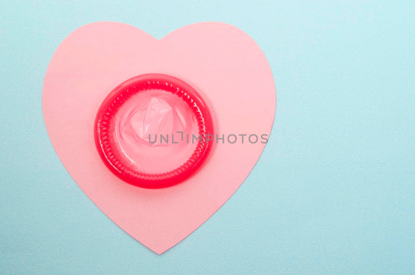 Pink condom unpackage on pink paper heart shape with copy space for your text or message.