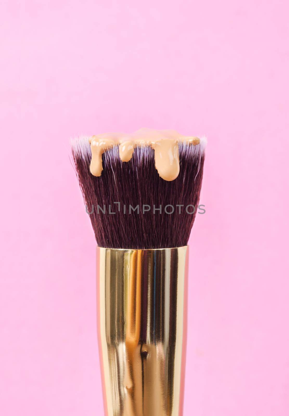 pouring liquid beige makeup foundation on a brush makeup with pink background.