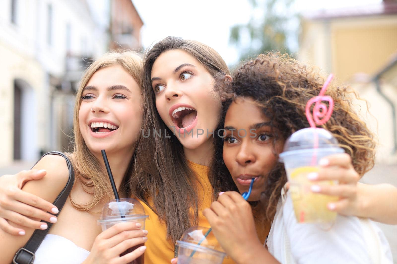Three trendy cool hipster girls, friends drink cocktail in urban city background
