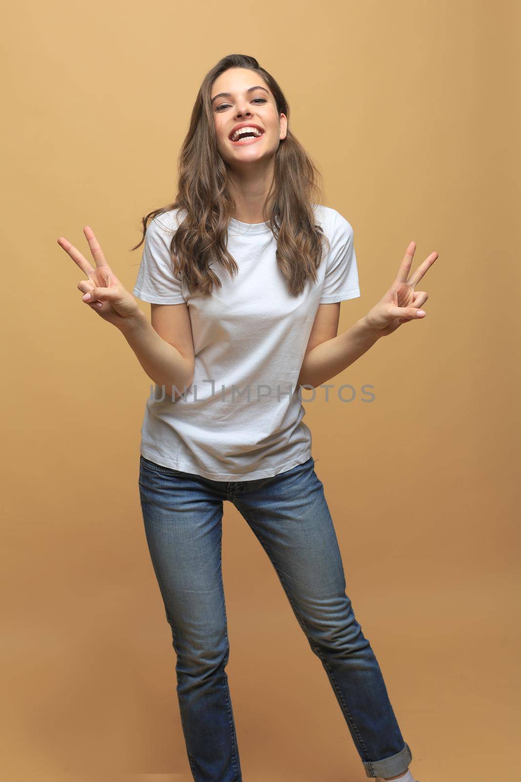 Lovely young woman showing victory or peace sign, isolated over beige background. by tsyhun