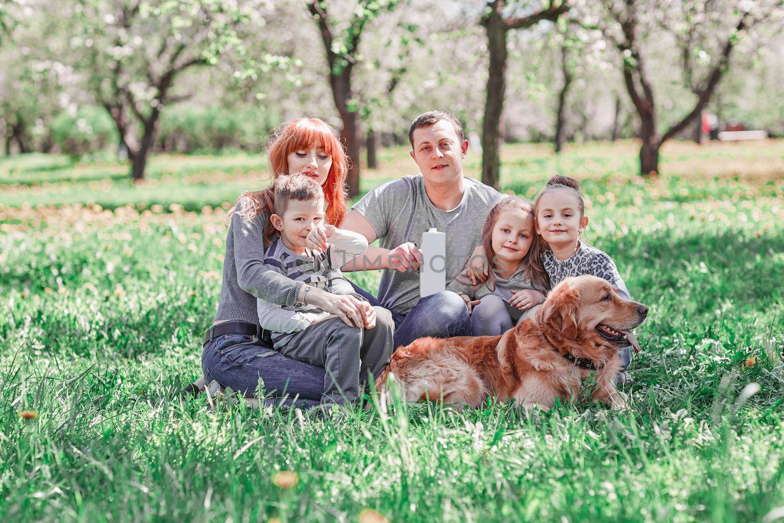 parents, children and their pet sitting on the lawn on a summer day. the concept of a healthy lifestyle