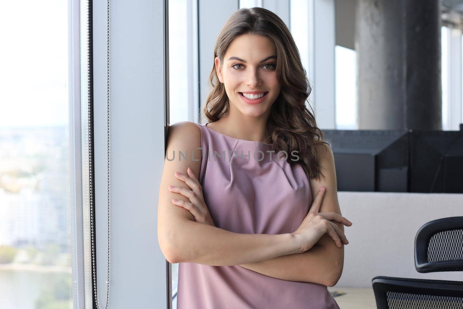 Attractive business woman looking at camera and smiling while standing in the office near the window.