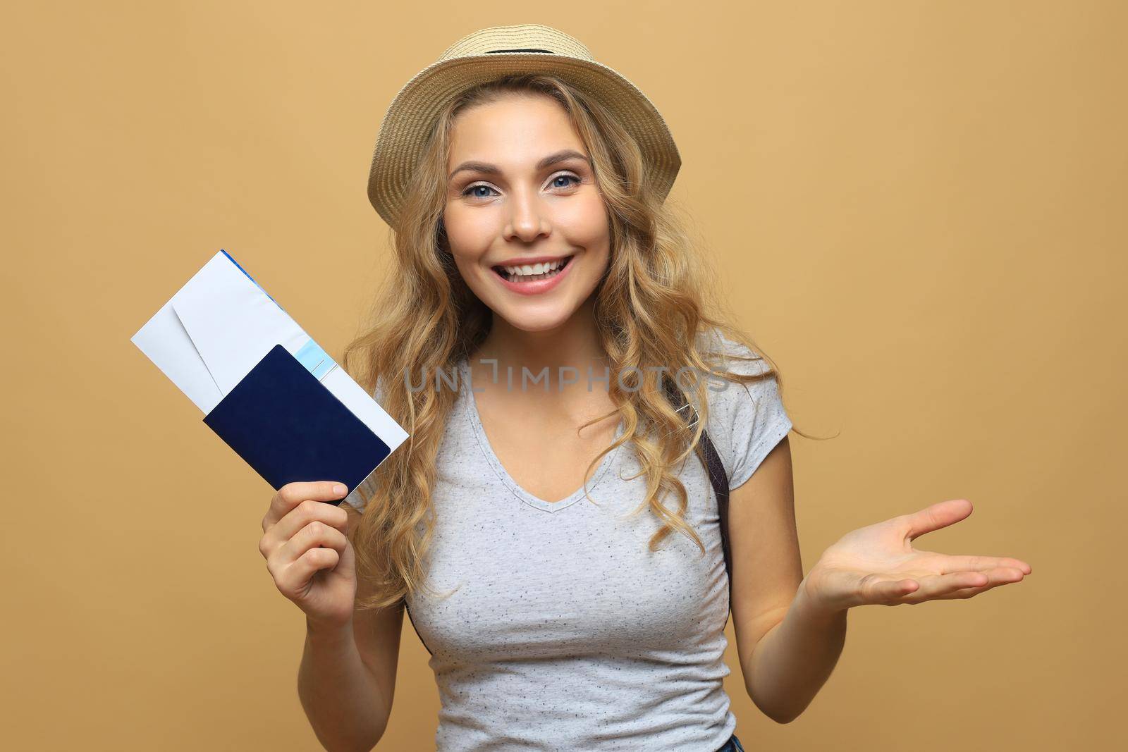 Beautiful blonde woman wearing summer clothes posing with passport with tickets over beige background