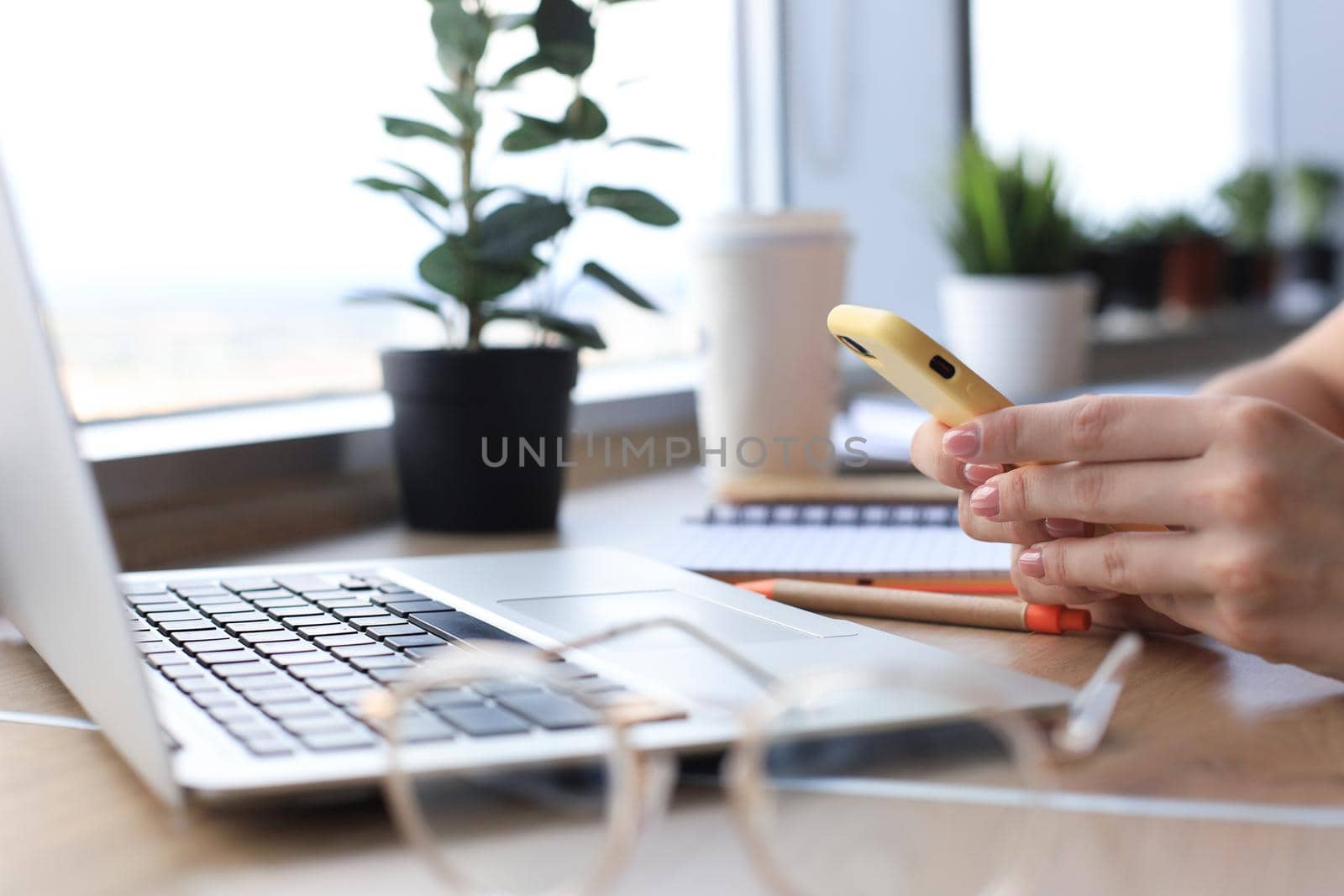 Close-up of businesswoman hands using smart phone while working on laptop