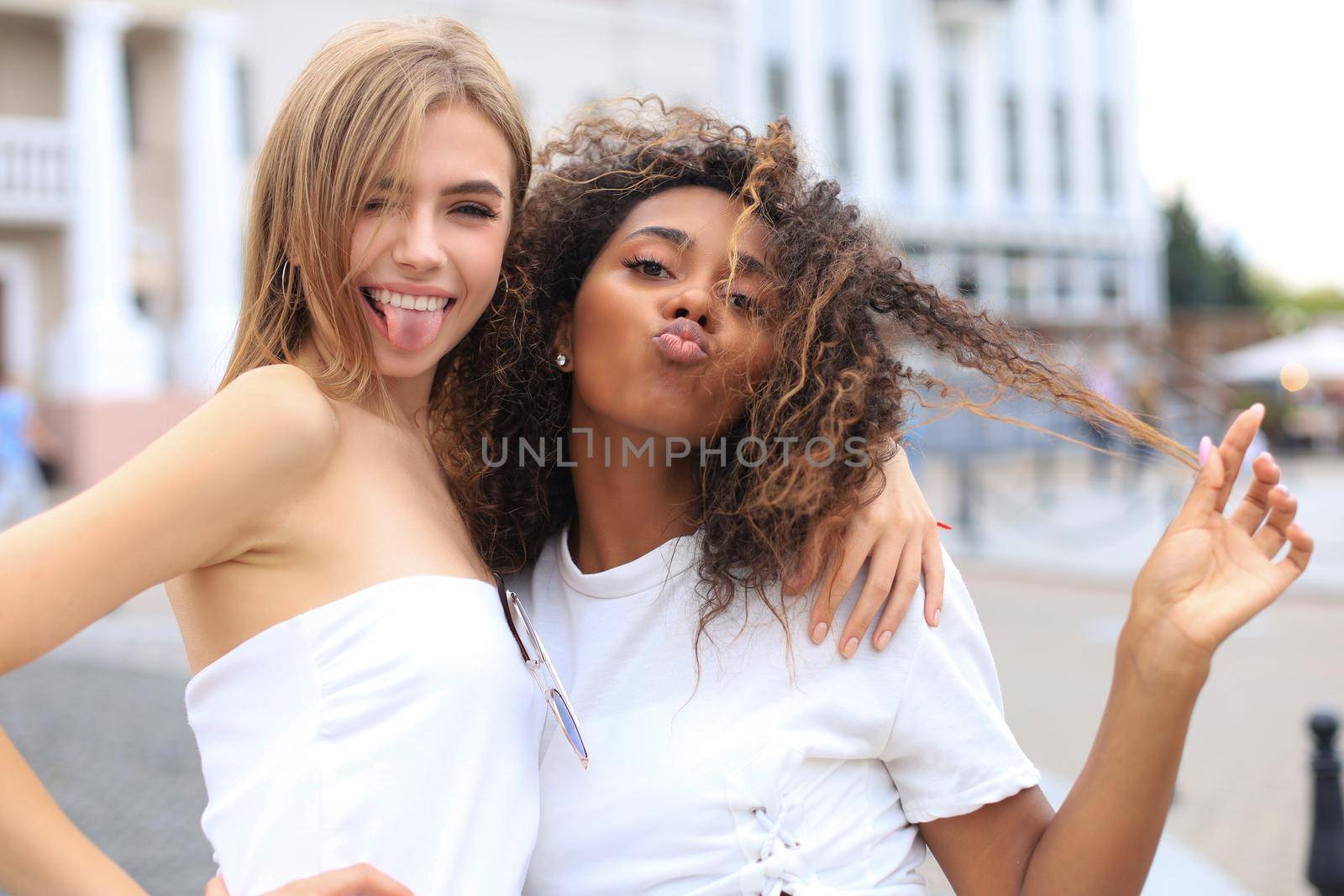 Young smiling hipster women in summer clothes posing on street.Female showing positive face emotions