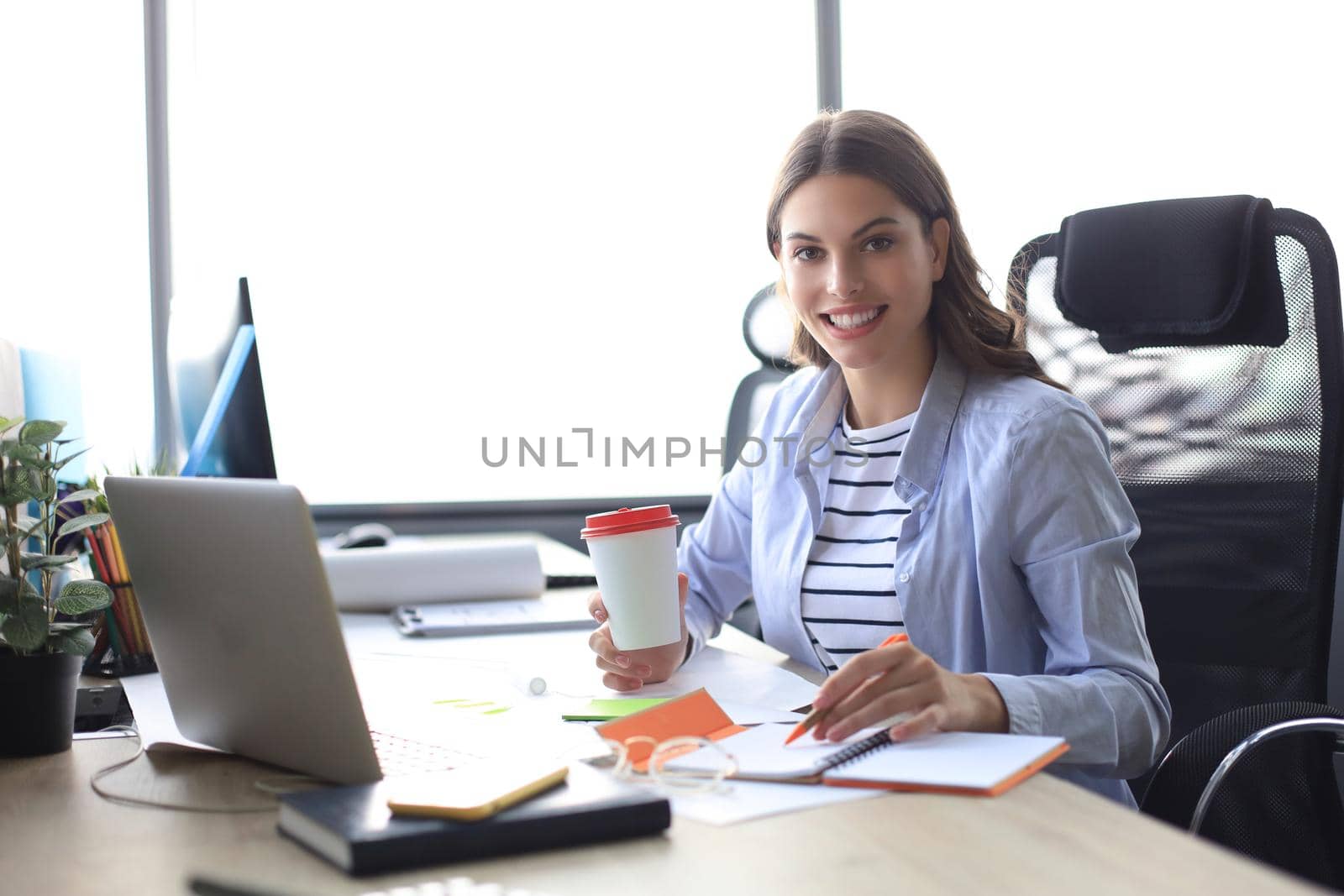 Beautiful smiling business woman is sitting in the office and looking at camera by tsyhun