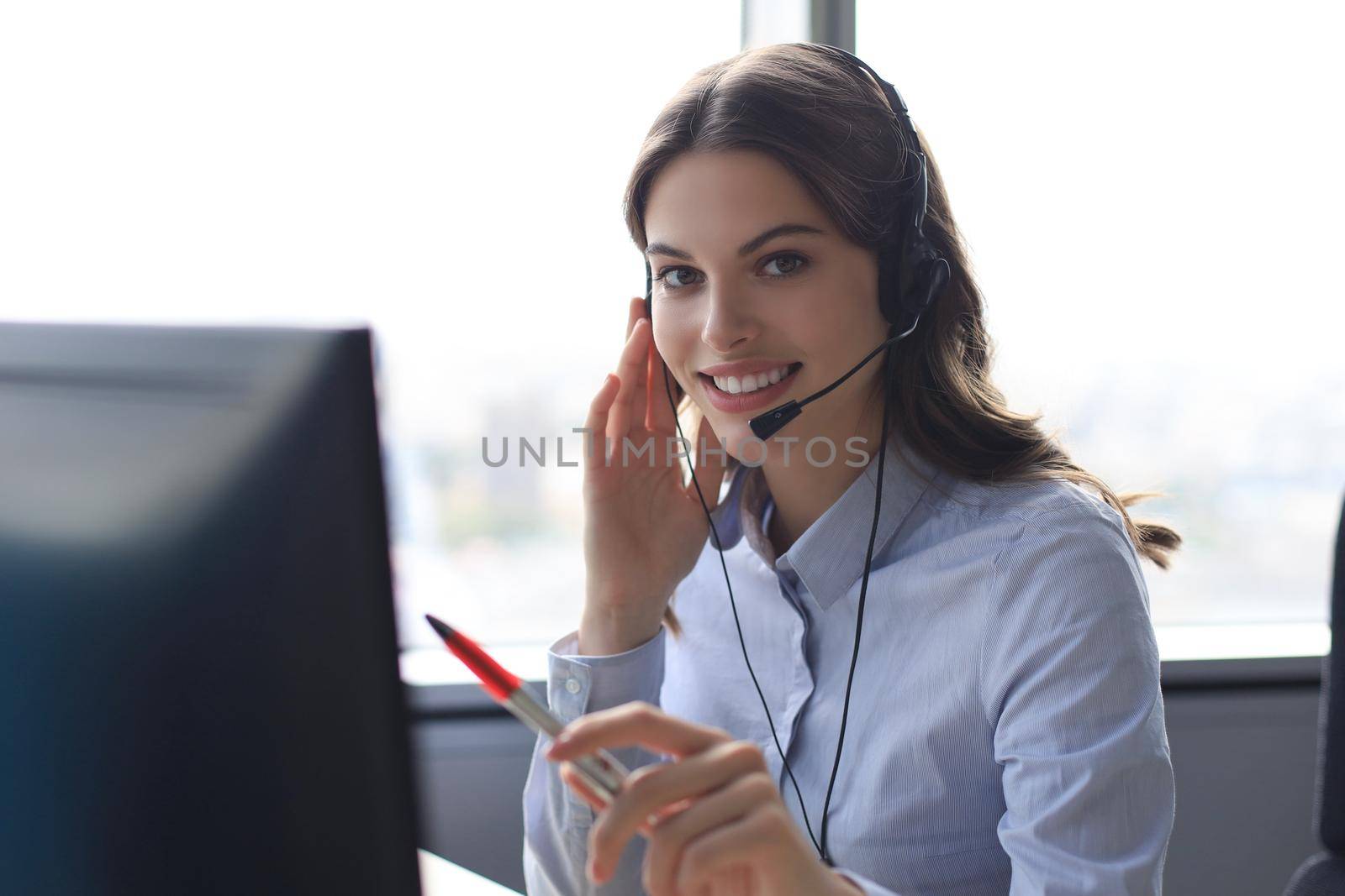Beautiful smiling call center worker in headphones is working at modern office.