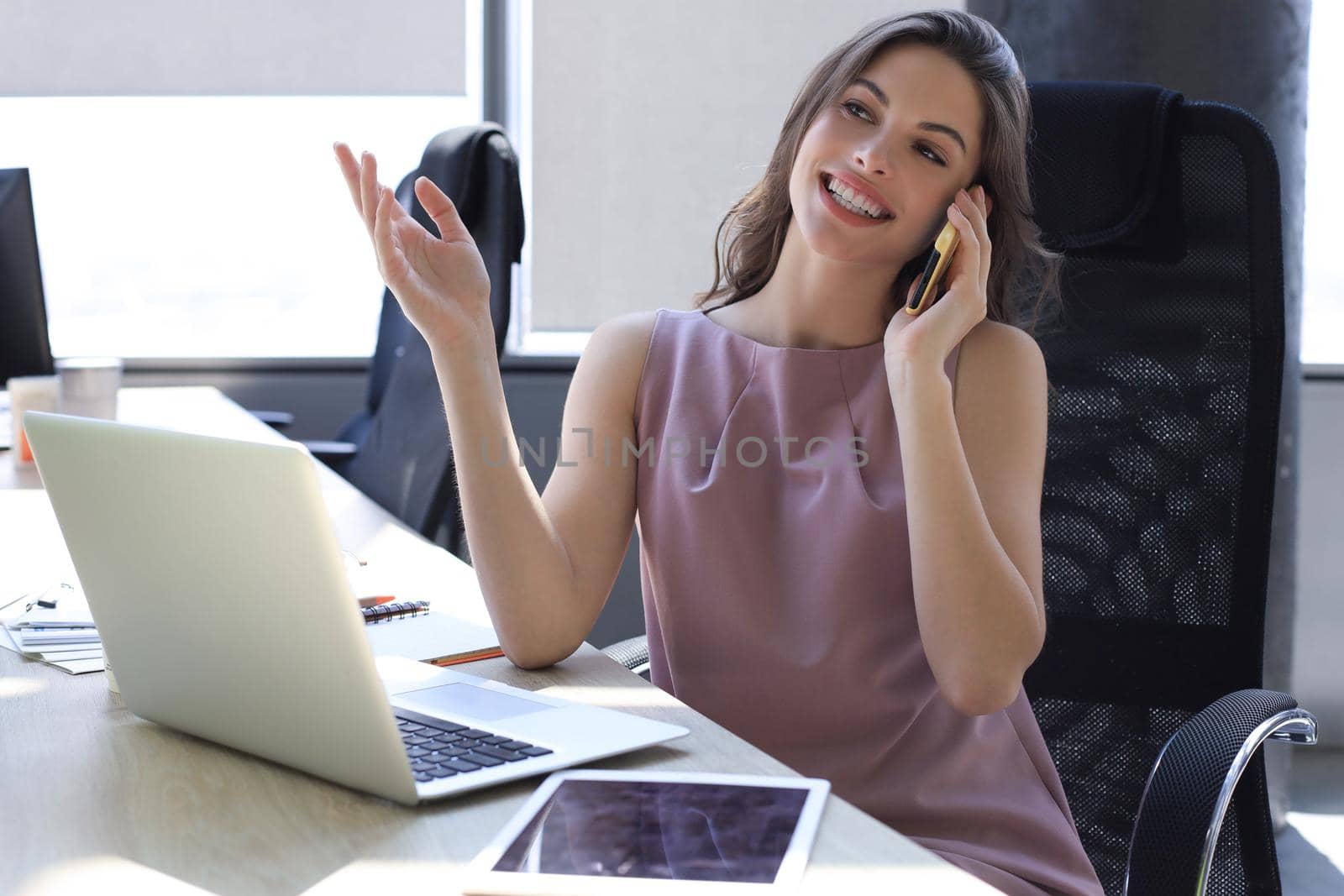 Attractive business woman talking with collegues on the mobile phone while sitting in the office desk.