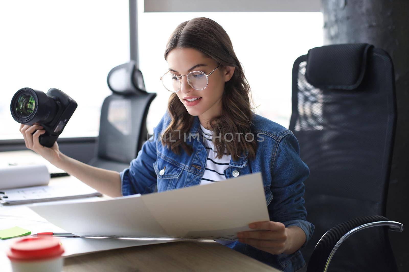 Young architect holding digital camera and looking on blueprint while working in the creative office