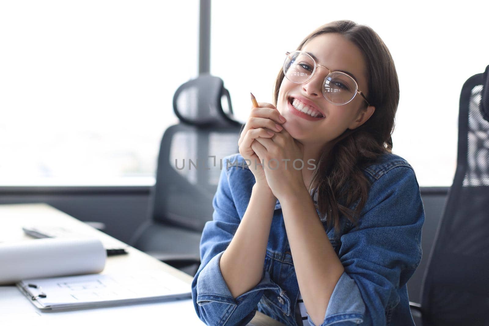 Beautiful young woman is sitting in the office and looking at camera