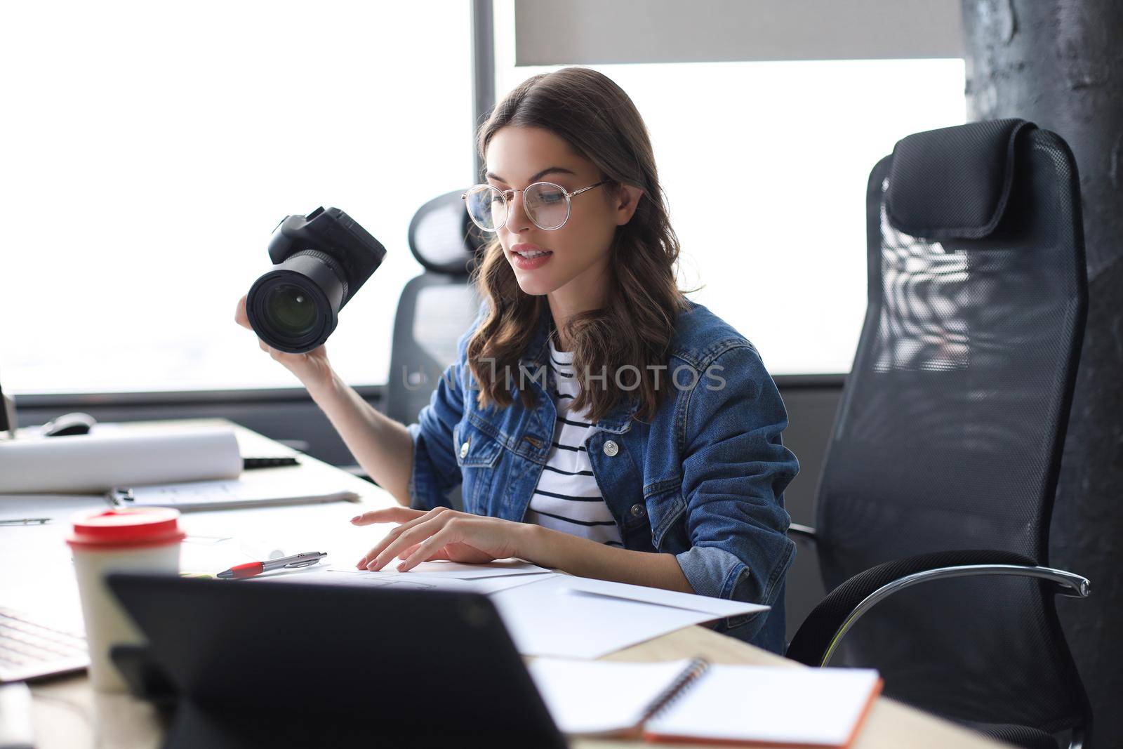 Young architect holding digital camera and looking on blueprint while working in the creative office