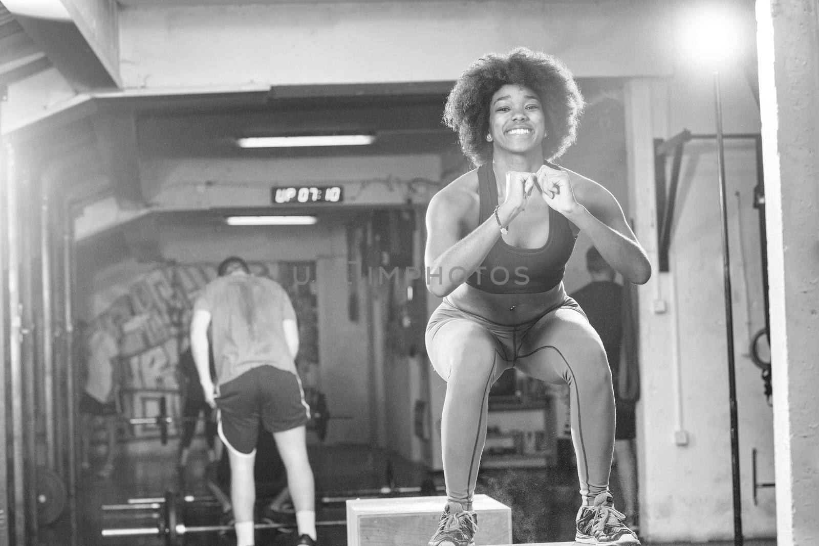 Fit young african american woman box jumping at a crossfit style gym. Female athlete is performing box jumps at gym.