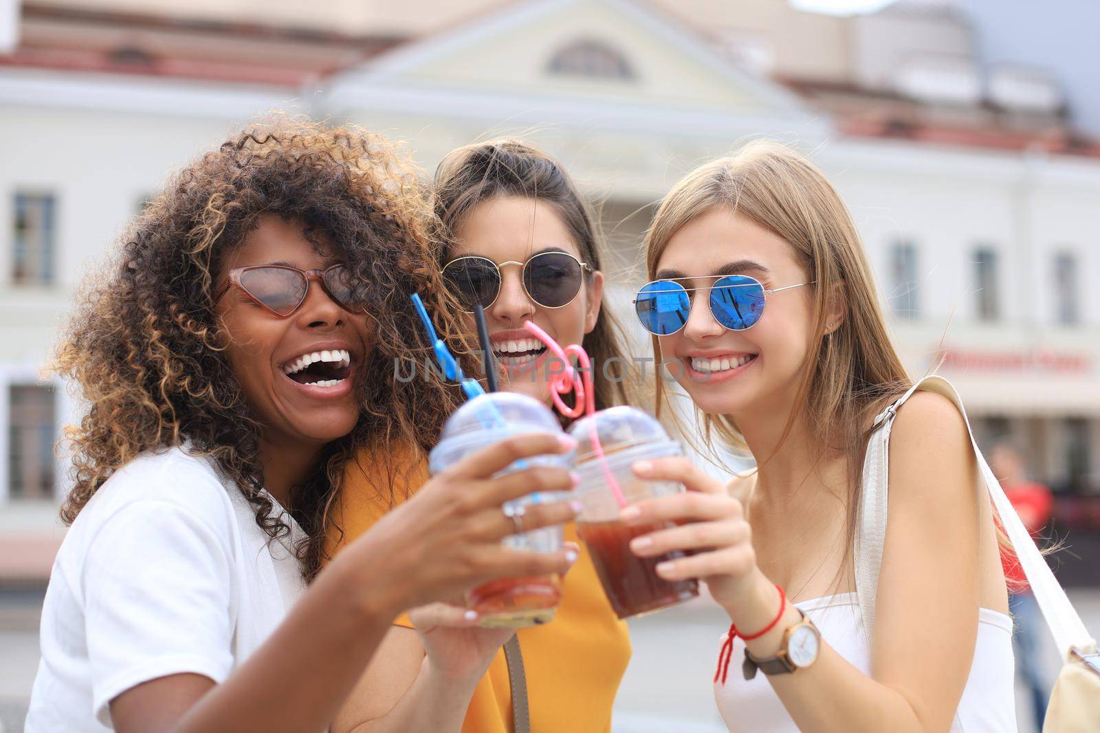 Three trendy cool hipster girls, friends drink cocktail in urban city background