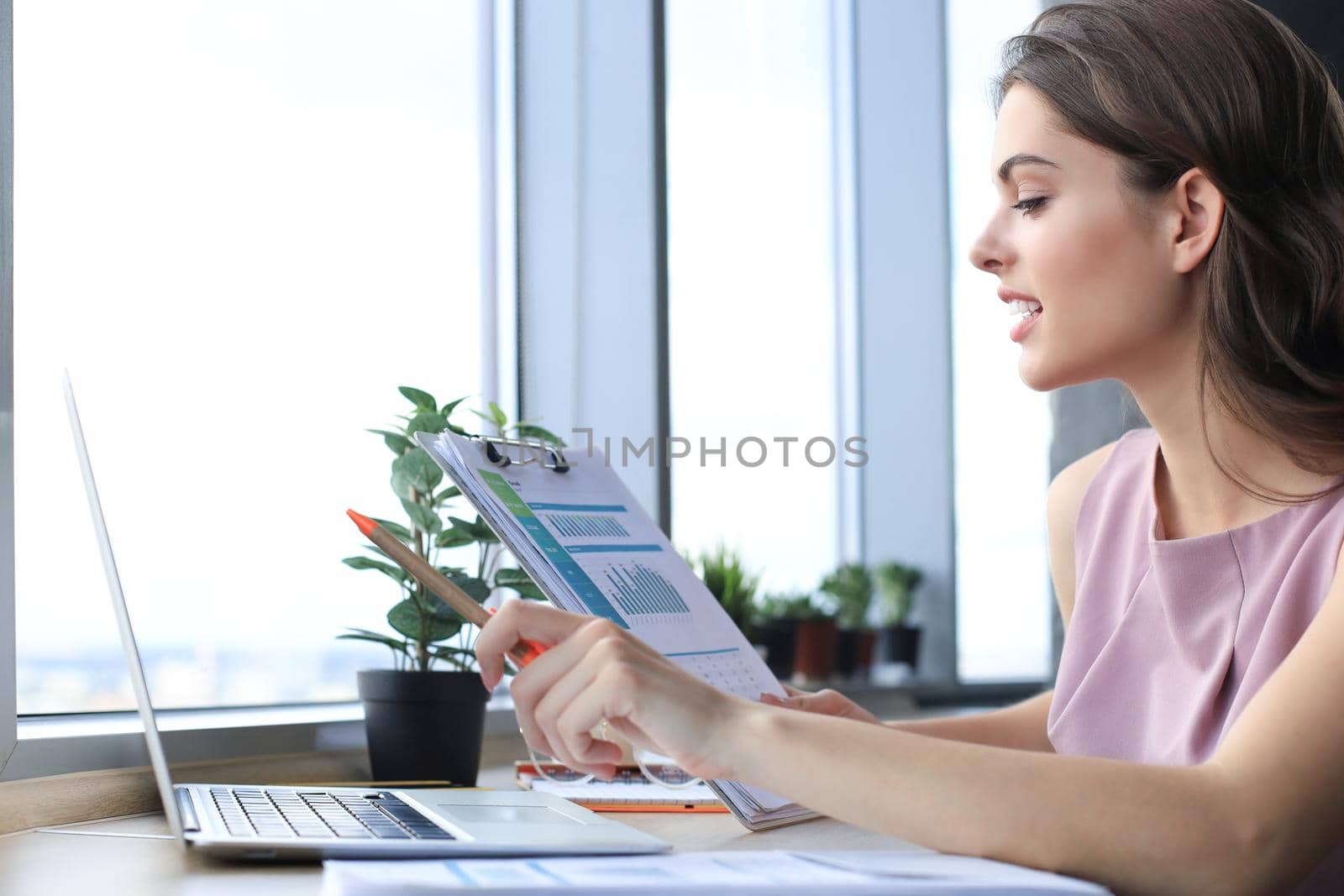 Beautiful young woman using laptop and looking at it while sitting at her working place