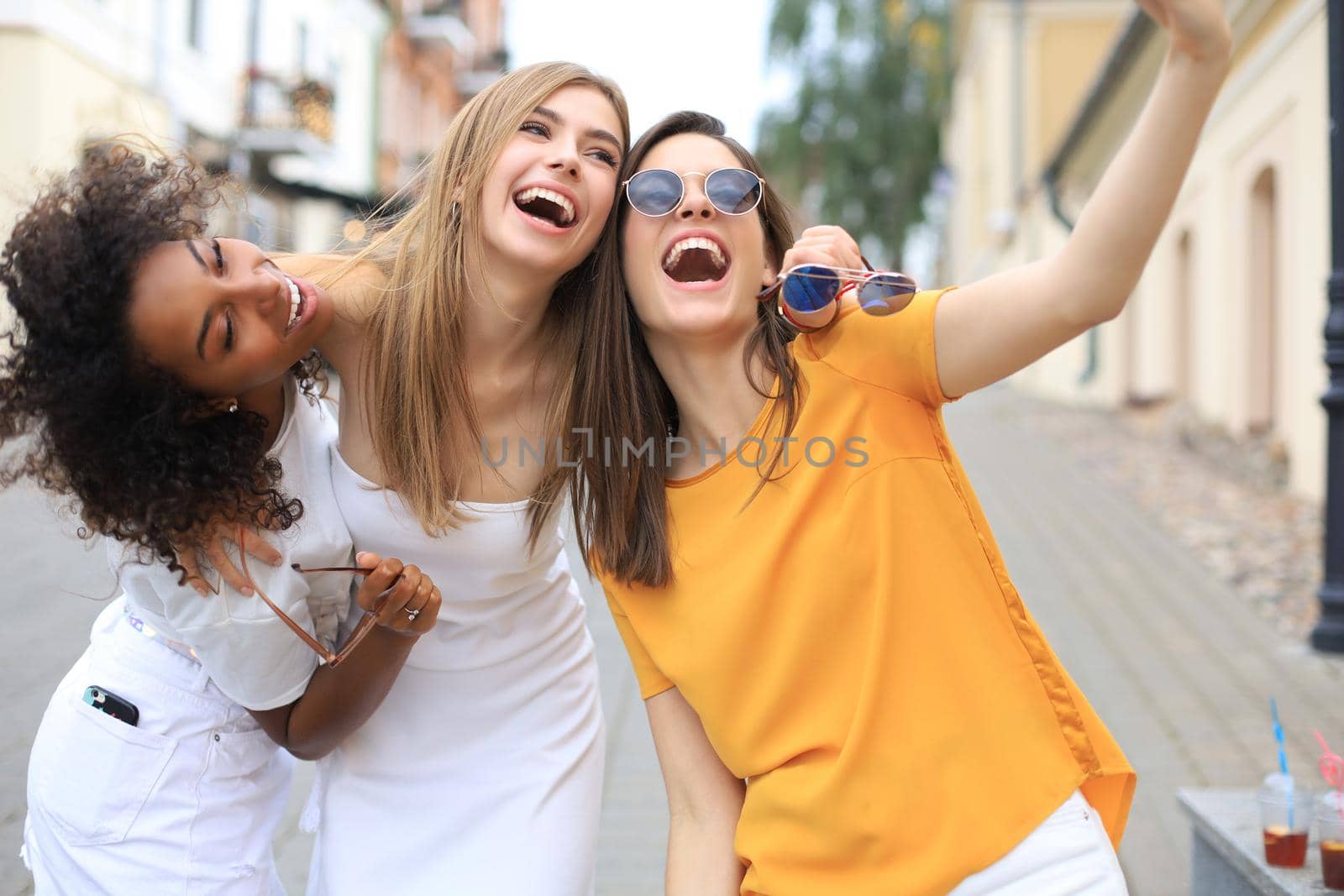 Three cute young girls friends having fun together, taking a selfie at the city