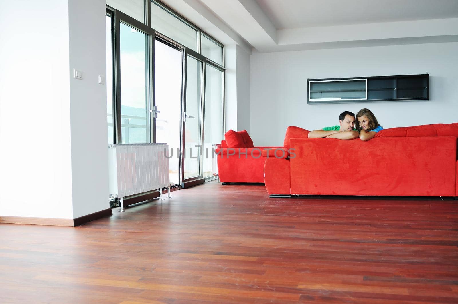 happy couple relaxing on red sofa in big bright new apartment