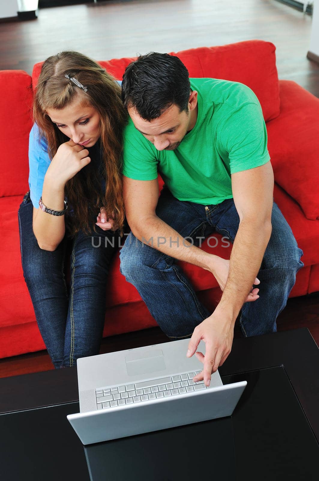 happy couple have fun and work on laptop at home on red sofa by dotshock