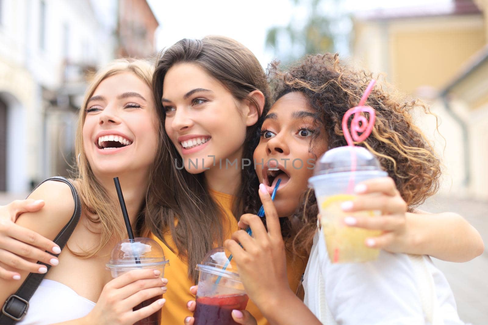 Three trendy cool hipster girls, friends drink cocktail in urban city background