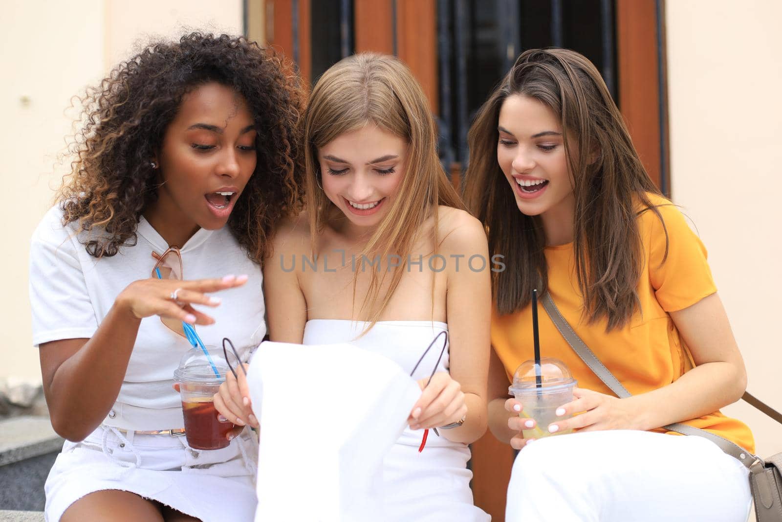 Beautiful girls with shopping bag discussing purchases and smiling while walking in city