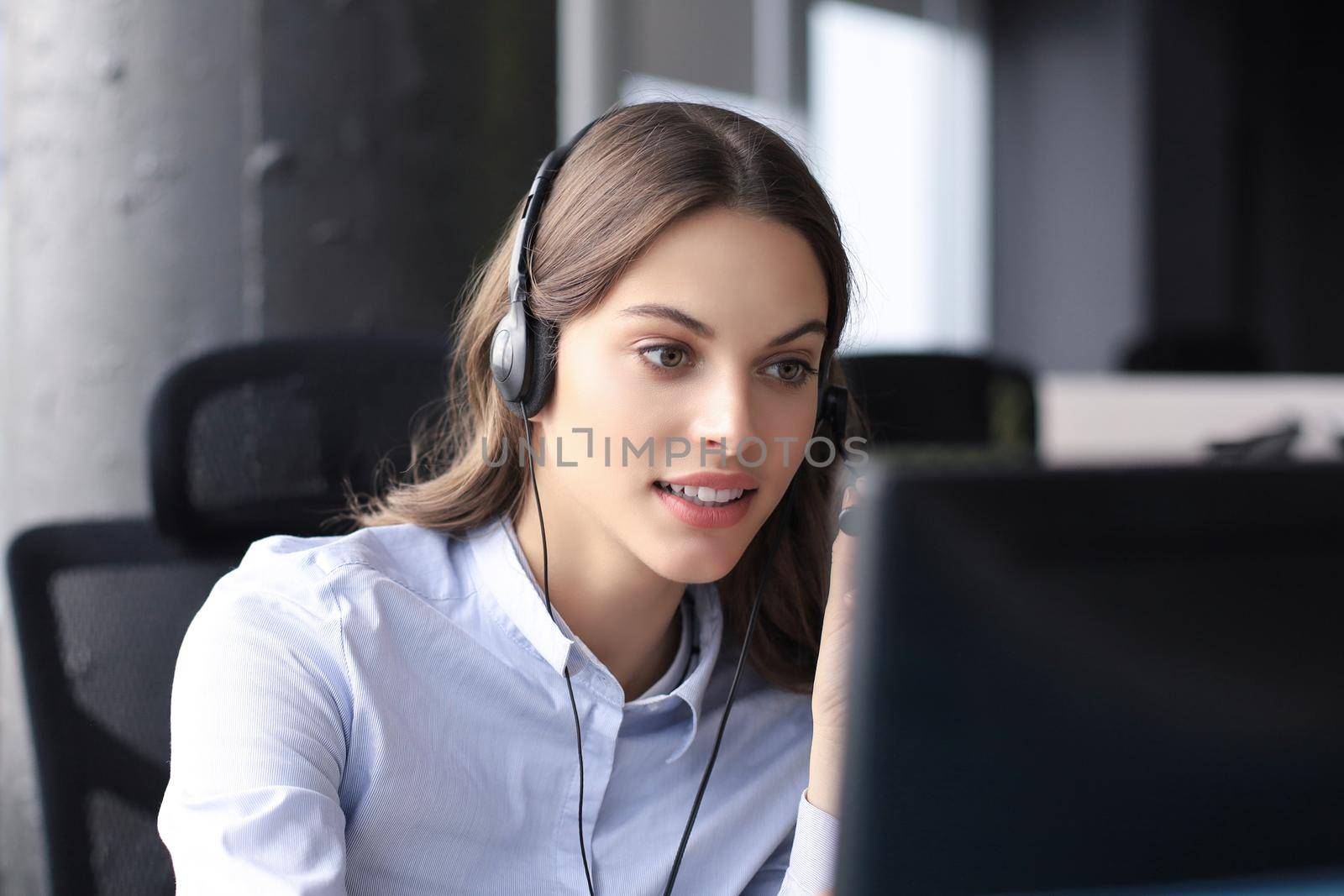 Beautiful smiling call center worker in headphones is working at modern office.
