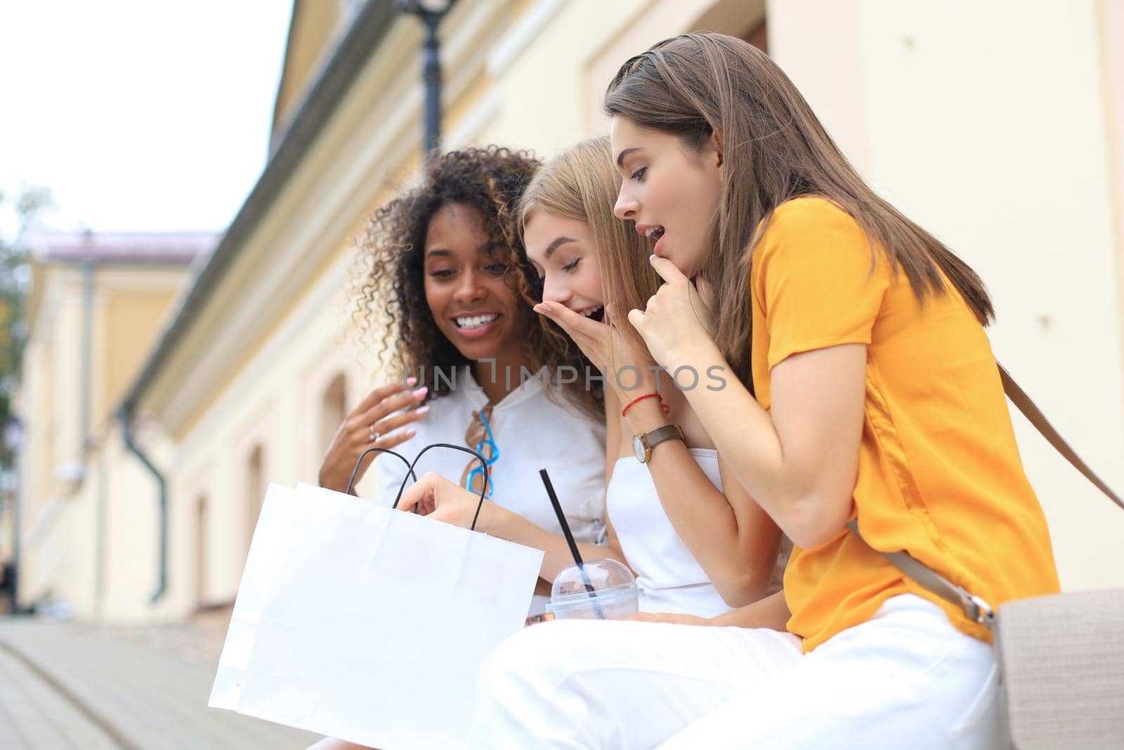 Beautiful girls with shopping bag discussing purchases and smiling while walking in city