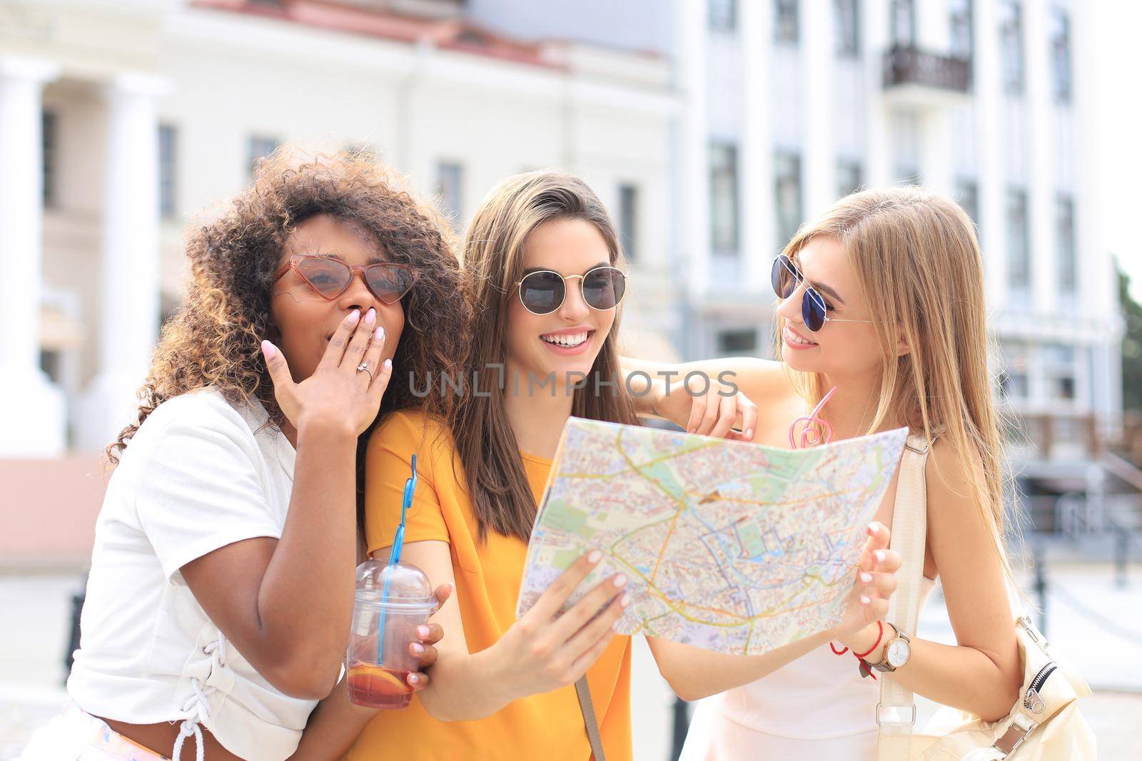 Photo of three girls enjoying sightseeing outdoor. Beautiful female tourists exploring city with map