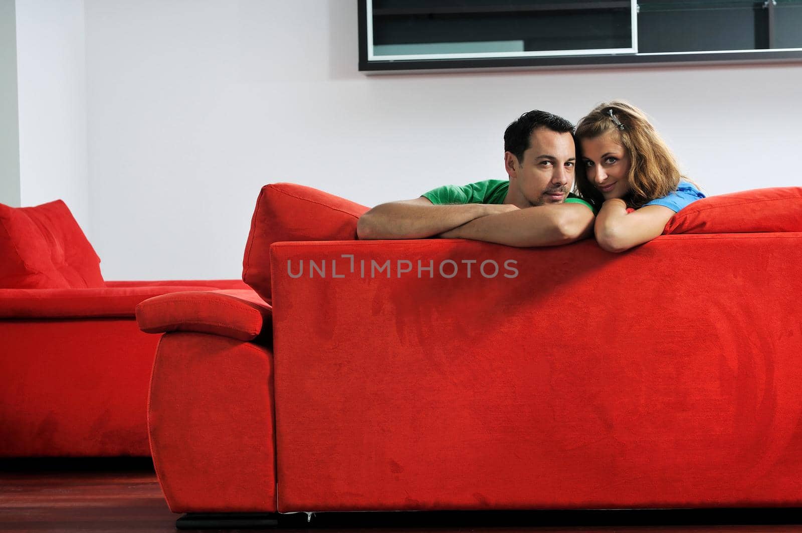 happy couple relaxing on red sofa in big bright new apartment