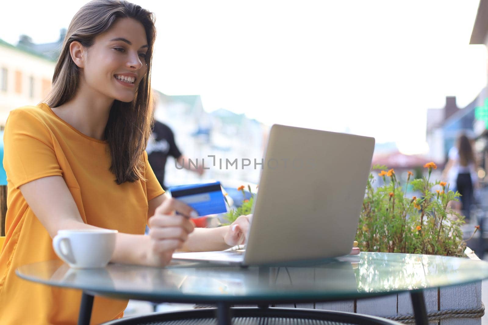 Happy natural brunette using credit card and laptop in cafe outdoors
