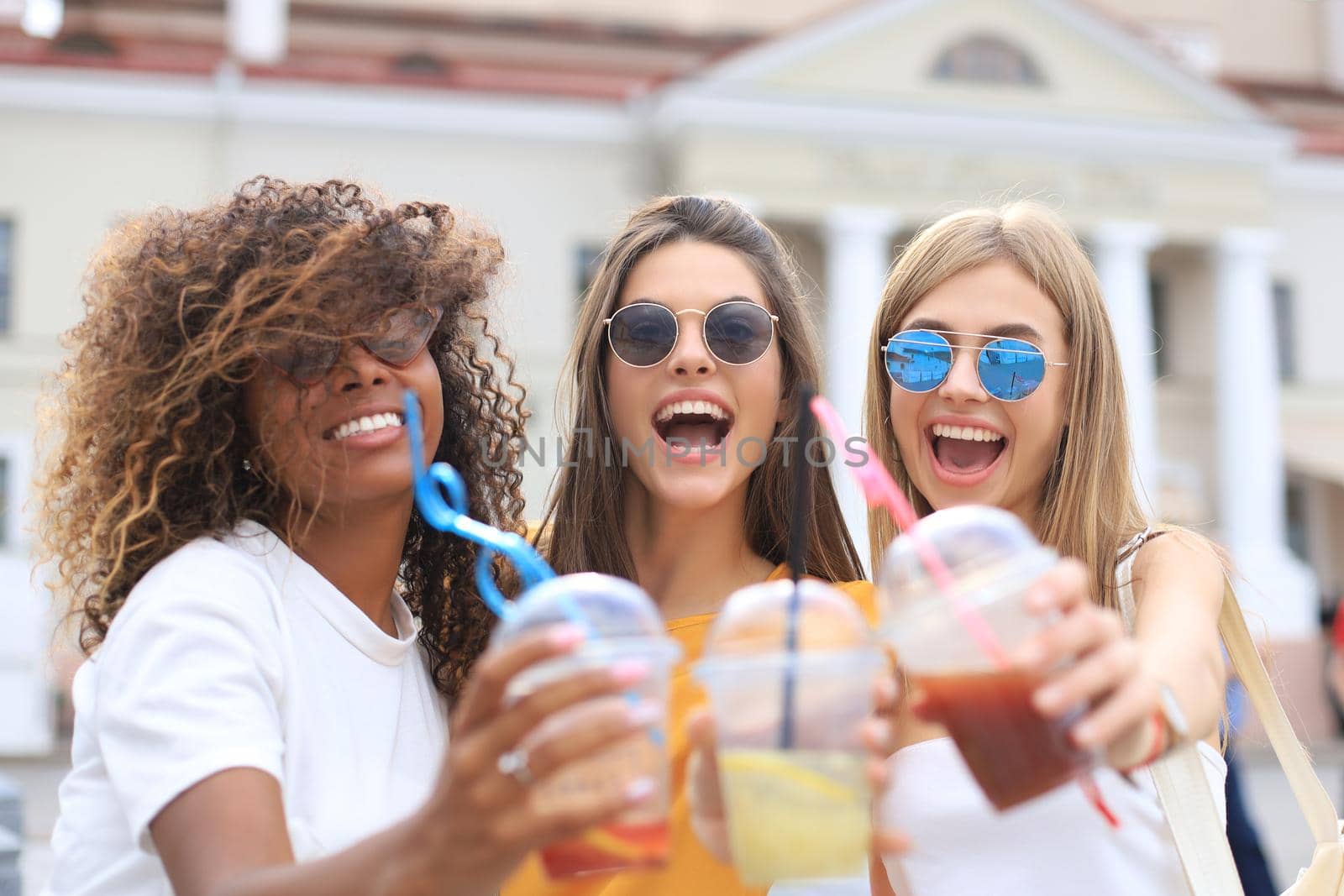 Three trendy cool hipster girls, friends drink cocktail in urban city background