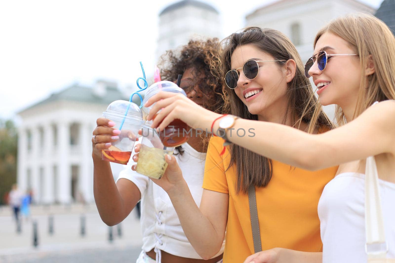 Three trendy cool hipster girls, friends drink cocktail in urban city background
