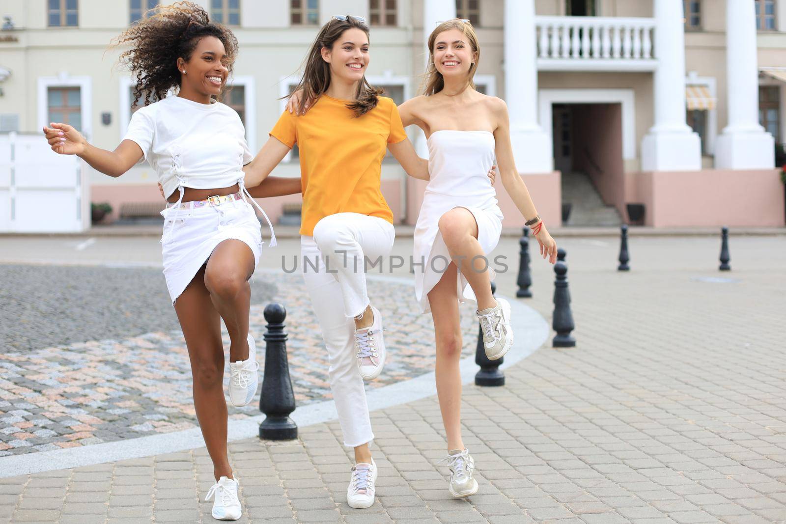 Three young smiling hipster women in summer clothes posing on street.Female showing positive face emotions. Dancing