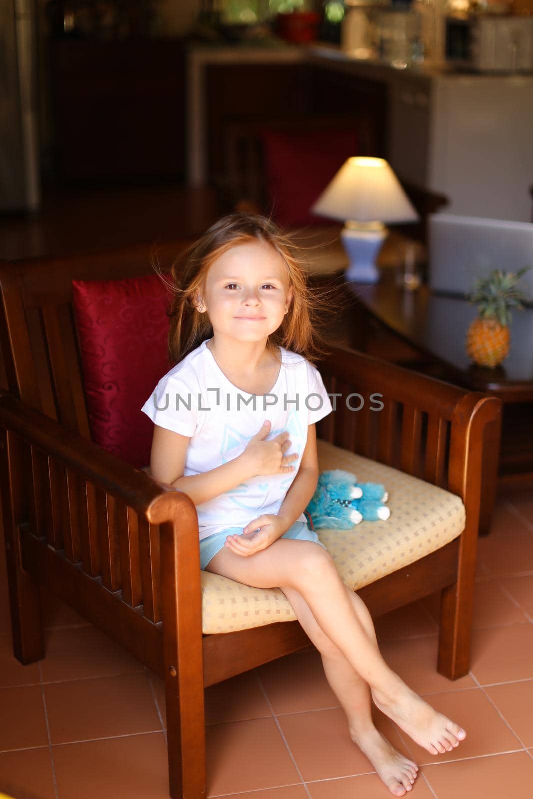 Little american female kid sitting with toy in wooden chair. Concept of kid model and wood in interior.