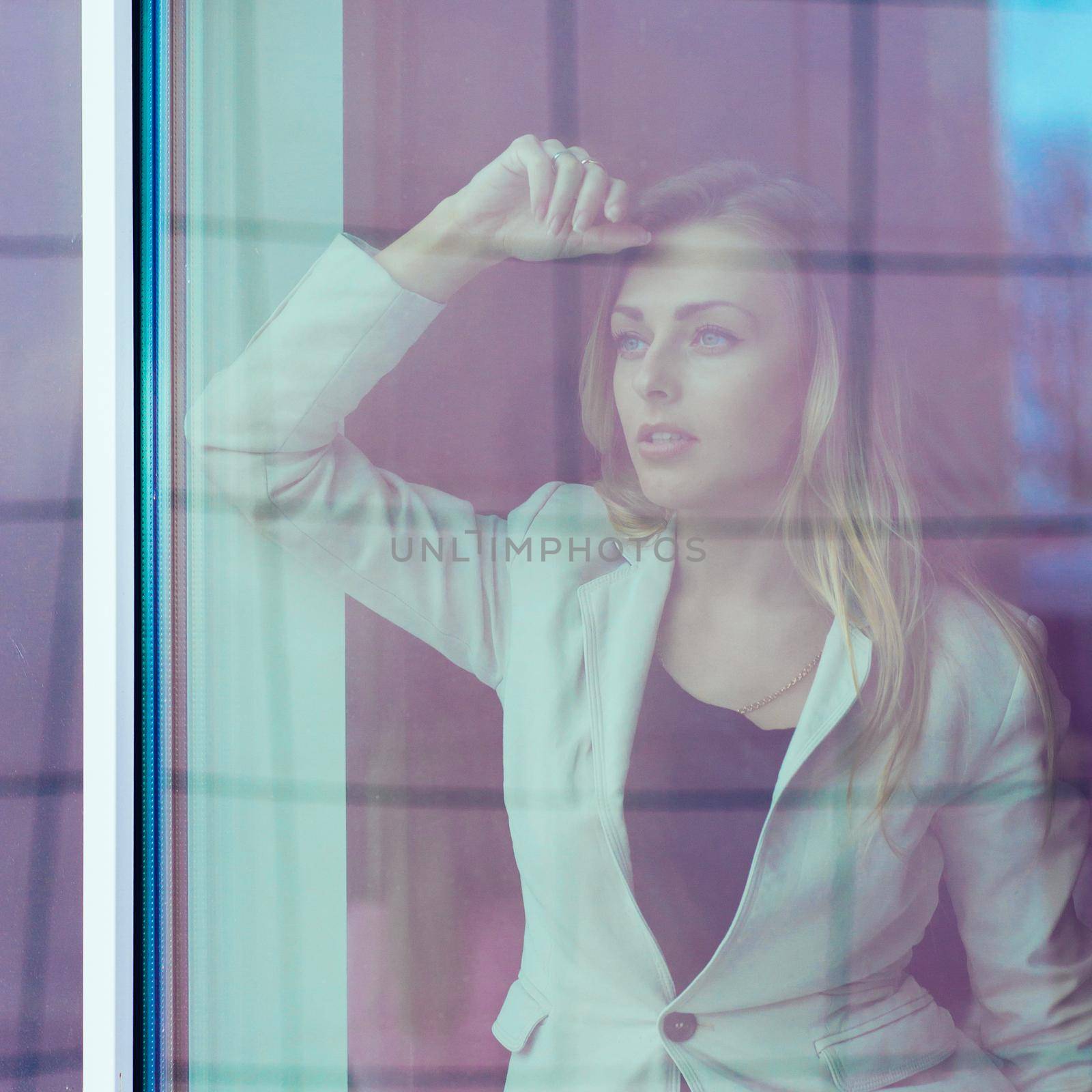 photo from behind the glass: successful woman leader looks out the window of his personal office