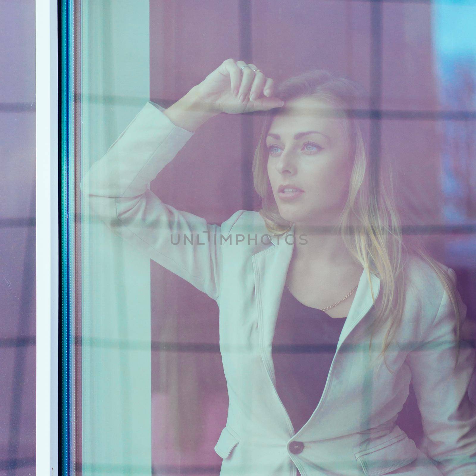 photo from behind the glass: successful woman leader looks out the window of his personal office