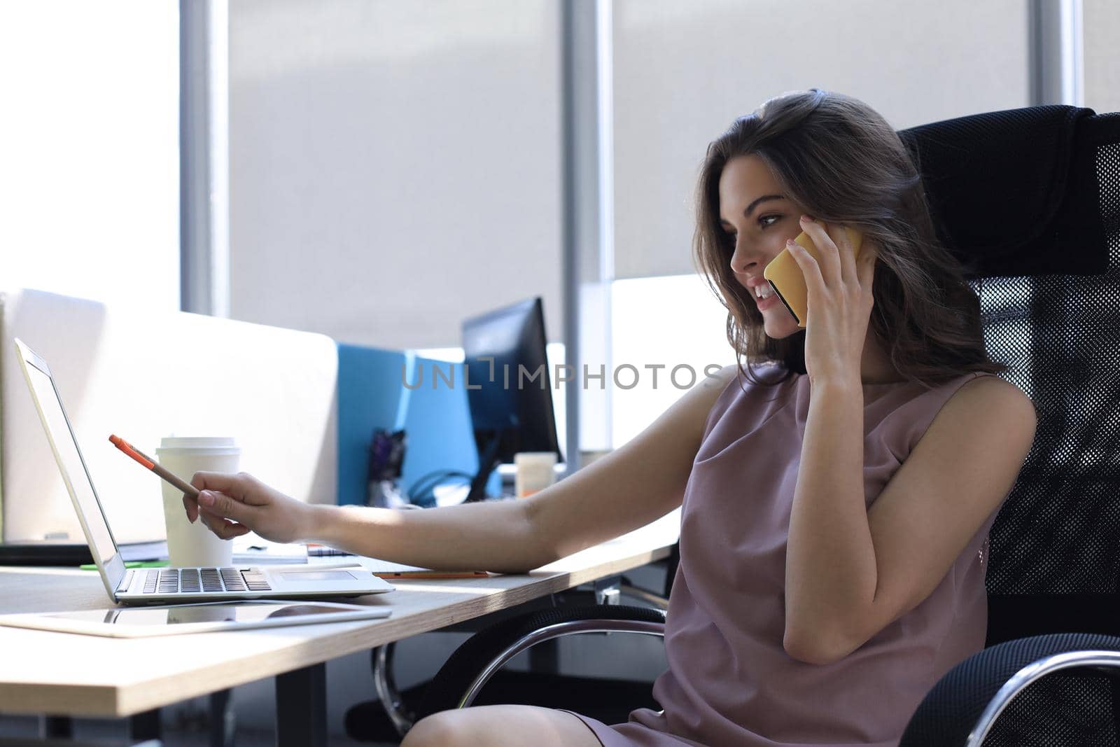 Attractive business woman talking with collegues on the mobile phone while sitting in the office desk.