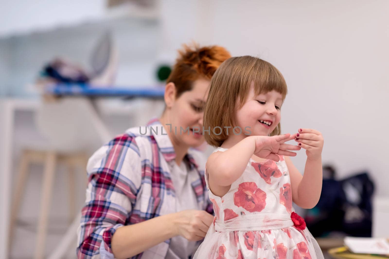 family having fut on beautiful evening  young mother helping cute little daughter while putting on a dress with red flowers for dancing at home