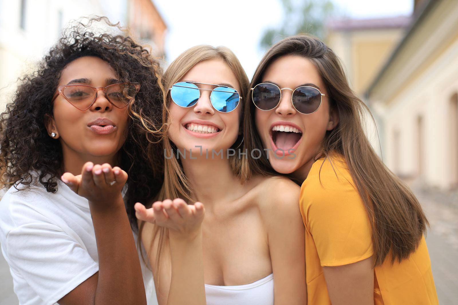 Three beauty women wearing summer clothes posing togeher in tke city and looking at the camera, sending kiss. by tsyhun