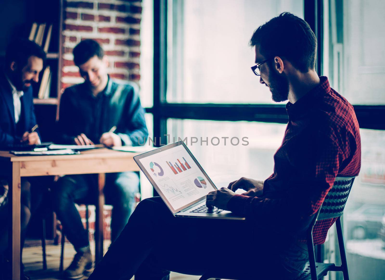 commercial Director working with financial graphs on the laptop in the office on the background of a successful business team