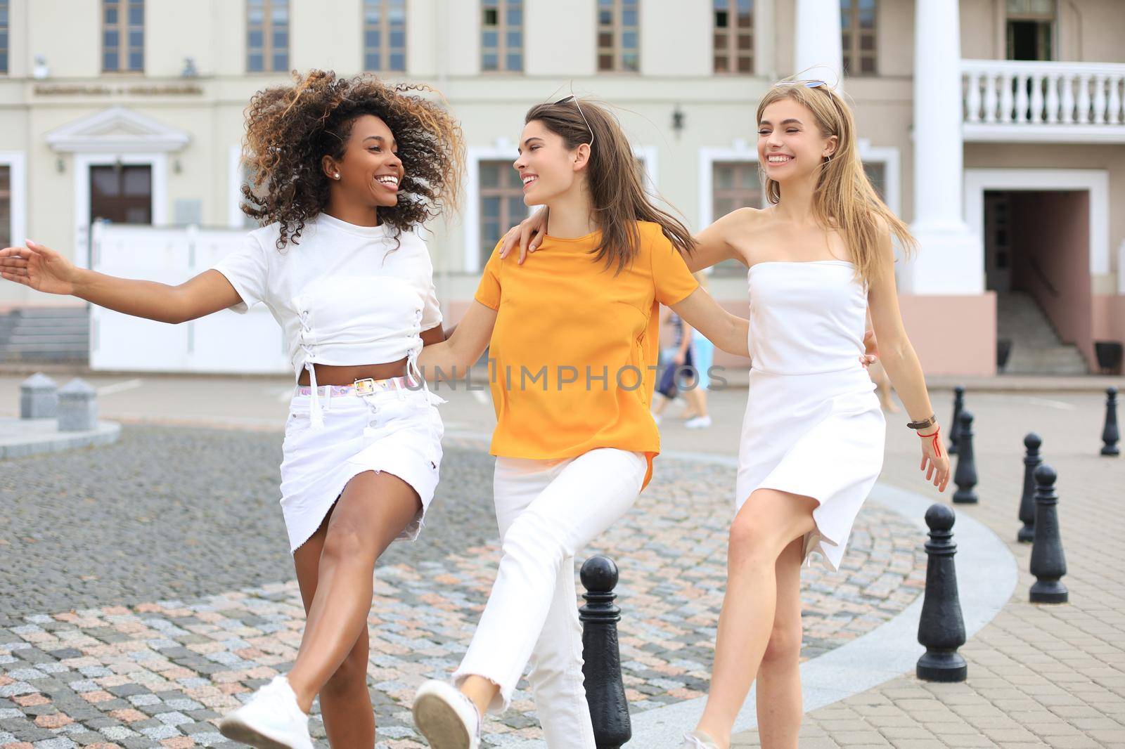 Three young smiling hipster women in summer clothes posing on street.Female showing positive face emotions. Dancing
