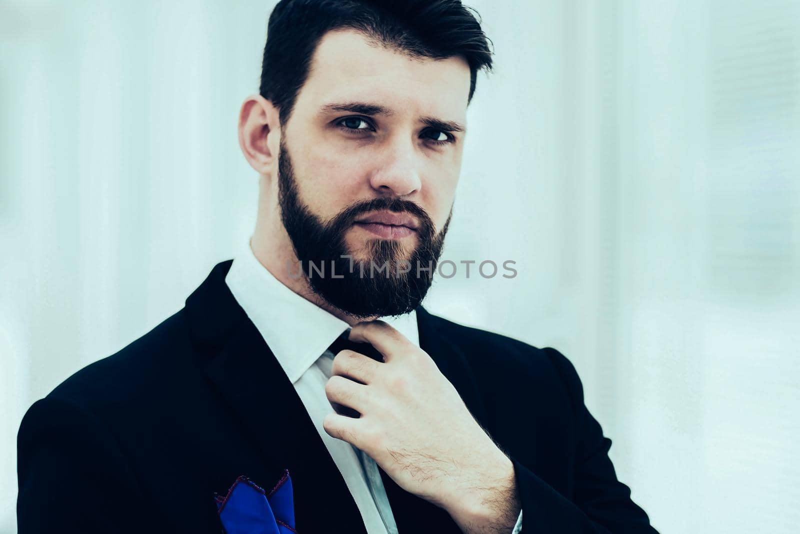 portrait of a successful businessman adjusting his necktie while standing near a window in bright office.the photo has a empty space for your text